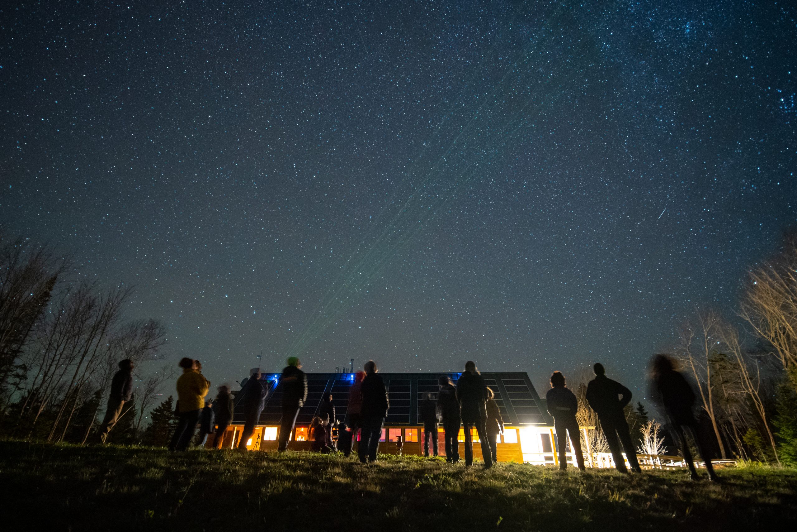 AMC's See the Dark Festival at Medawisla Lodge in the Maine Woods. Photo by Jenny Ward. People looking up at the night sky in front of Medawisla Lodge.